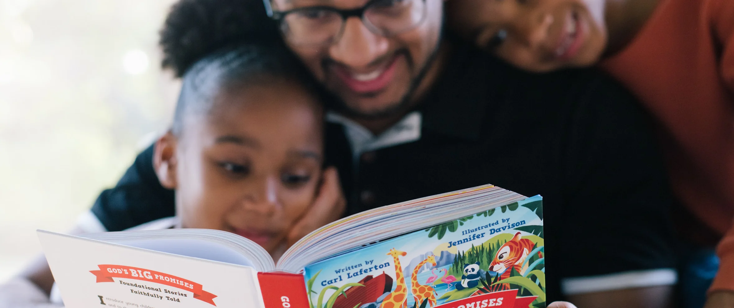A father and two children are gathered around reading God's Big Promises Bible Storybook
