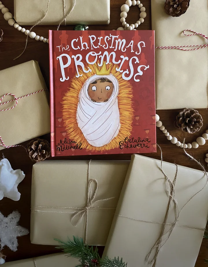 The Christmas Promise storybook, surrounded by wrapped presents and ornaments
