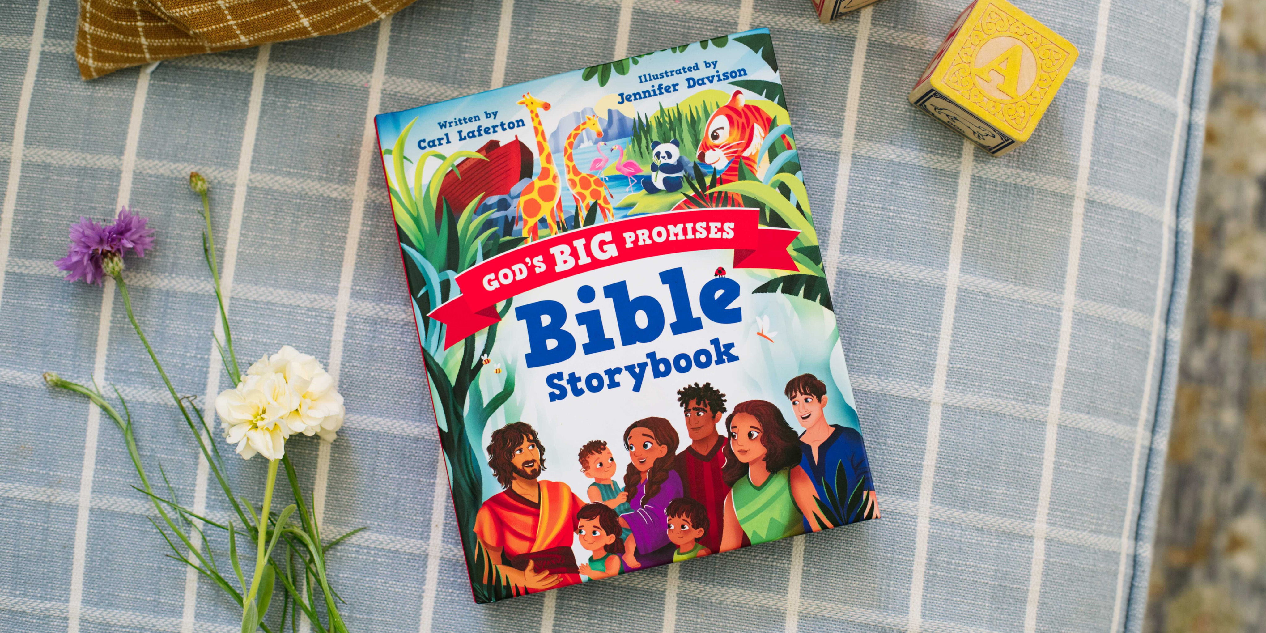 Photograph of God's Big Promises Bible Storybook on upholstery with flowers and children's blocks nearby. This photograph is located at the top of the Products page.