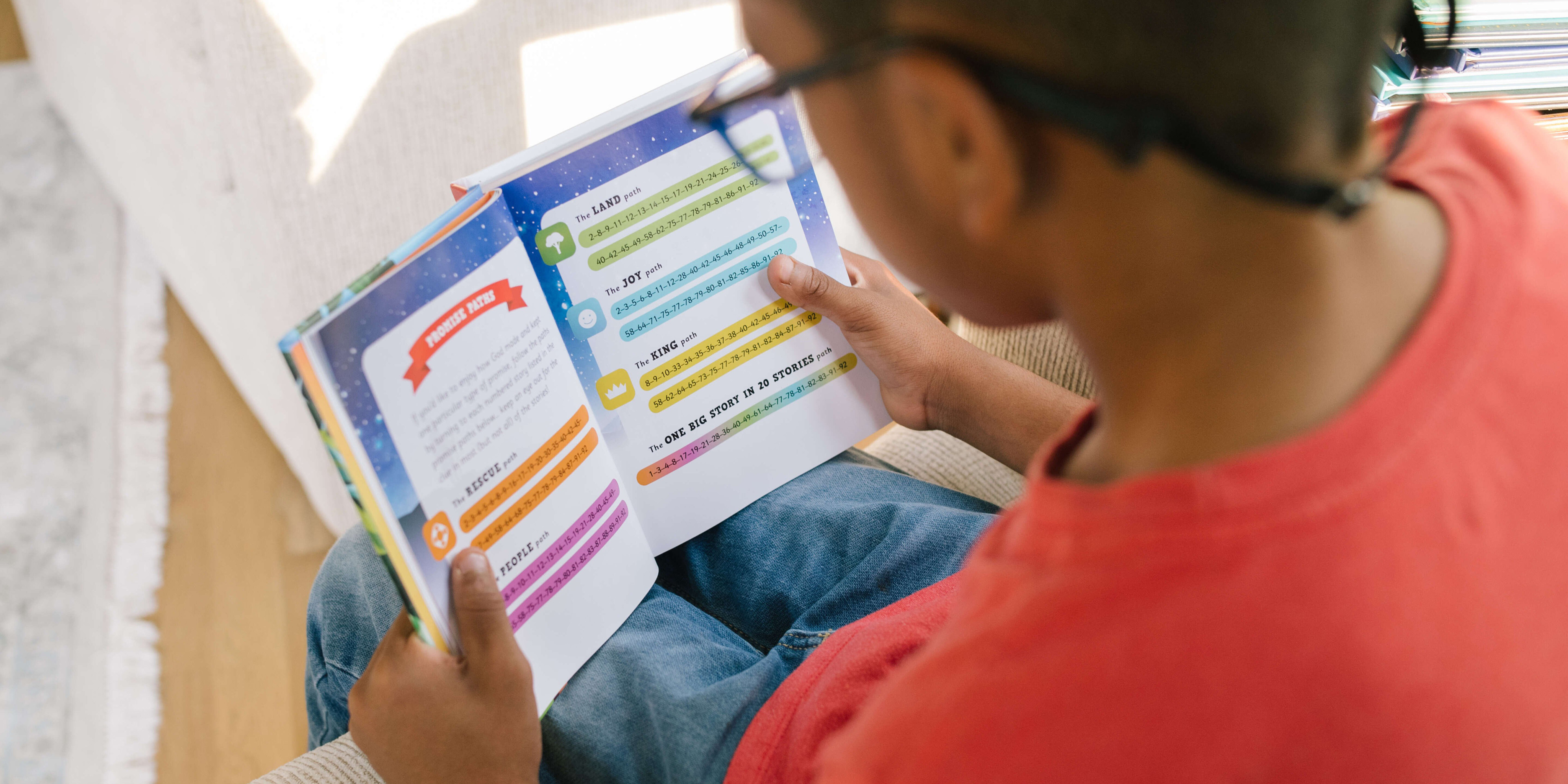 Photograph of a boy who is seated reading a page of God's Big Promises Bible Storybook which shows the various Promise Paths available in the Bible Storybook.